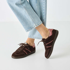 Brown sneakers with pink accents worn with light blue jeans on a white background