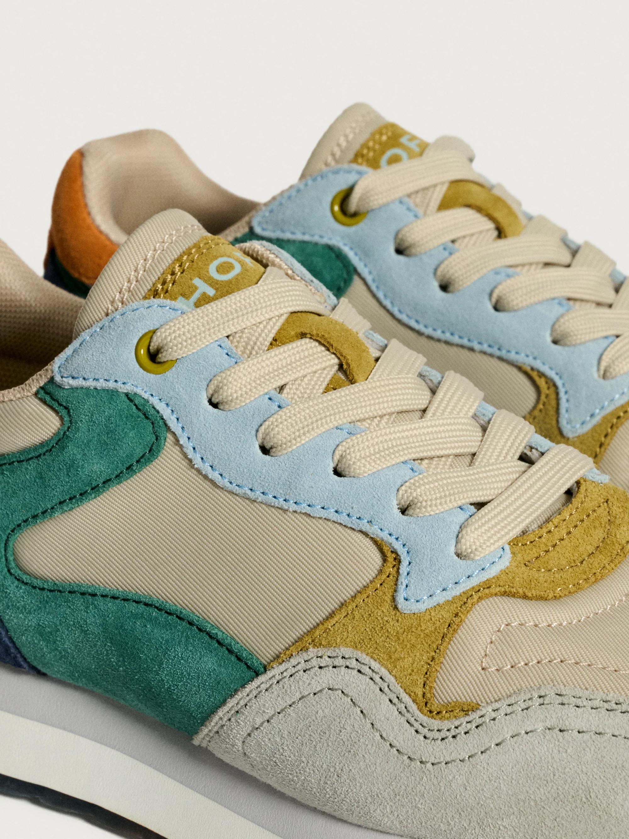 Colorful sneakers with a mix of beige, blue, green, and yellow on a light gray background